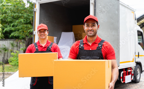 Two delivery workers dressed in shipping company uniforms were lifting or carrying boxes and standing behind a truck full of packages. During delivery to customers in transportation concept.