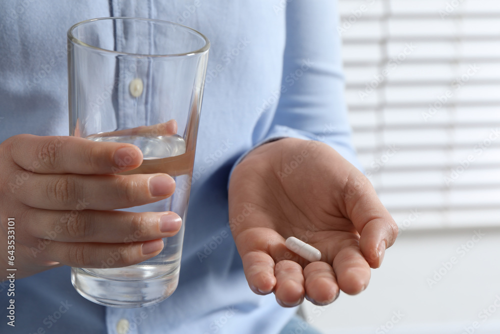 Woman with glass of water and pill on blurred background, closeup Woman with glass of water and pill on blurred background, closeup