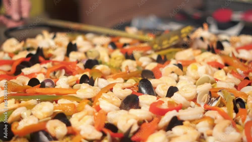 A huge, hot paella, skillfully made, waiting to be served to customers at a restaurant, carried with a slotted spoon.
