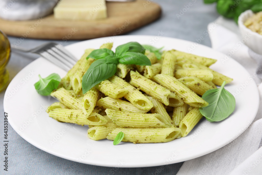 Delicious pasta with pesto sauce and basil on light grey table, closeup