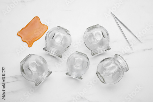 Glass cups, gua sha and tweezers on white marble table, flat lay. Cupping therapy