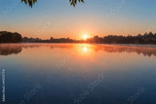 Pond with calm water and fog above water at sunrise