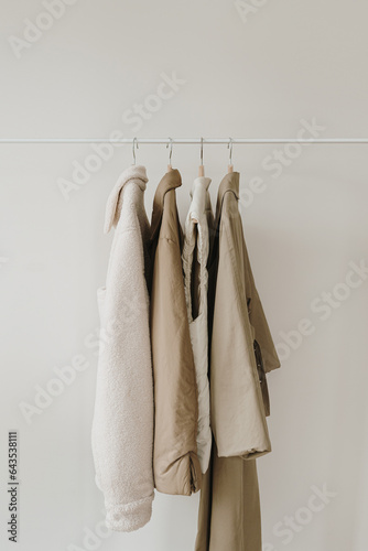 Warm autumn seasonal women's clothes on hanger over white wall. Neutral beige jackets and coat. Minimalist fashion clothes wardrobe