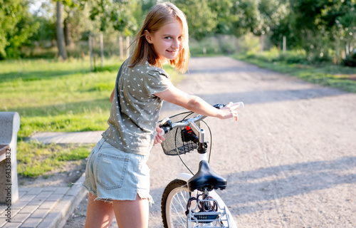 Quadro su tela Cute preteen girl with bycicle outdoors looking at camera and smiling