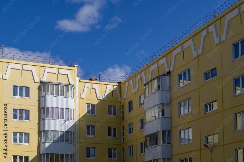 Multistory yellow residential building in a provincial town against a blue sky. Geometric lines, bright sunlight and hard shadows