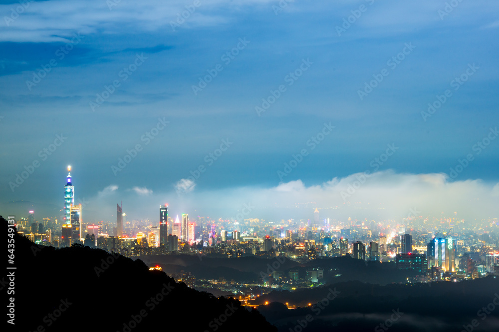 Nighttime Vista: Captivating City Lights and the Playful Dance of Clouds. View of the urban landscape from Dajianshan Mountain, New Taipei City, Taiwan.