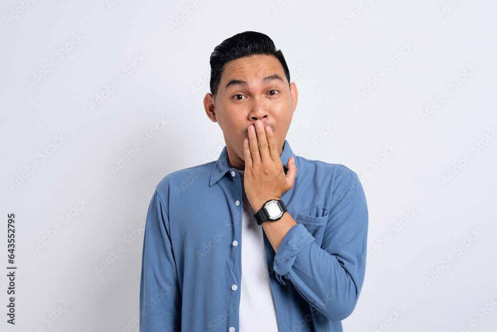 Surprised young Asian man in casual shirt covering mouth with hand, looking at camera with amazed facial expression isolated on white background Surprised young Asian man in casual shirt covering mouth with hand, looking at camera with amazed facial expression isolated on white background