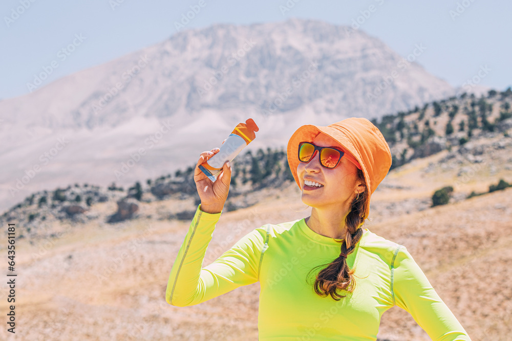 Pretty young woman biting on a energy sportive gel drink after a good hike in high mountains
