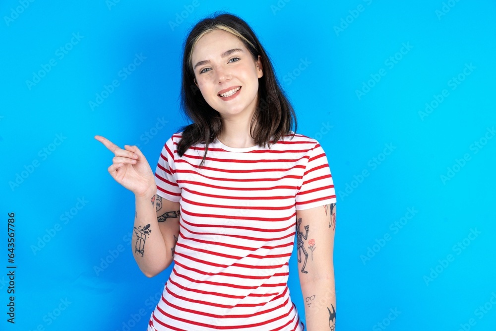 Young beautiful woman wearing striped t-shirt points to side on blank space demonstrates advertisement. People and promotion concept Young beautiful woman wearing striped t-shirt points to side on blank space demonstrates advertisement. People and promotion concept