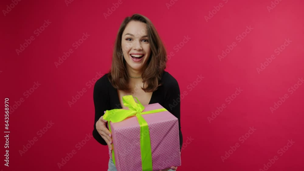 A gift on a red background falls into the hands of a young woman from above. Christmas, New Year, holiday A gift on a red background falls into the hands of a young woman from above. Christmas, New Year, holiday