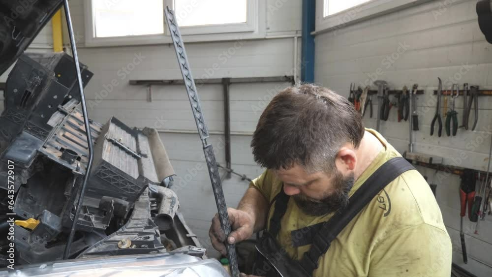 Professional bearded repairman fixing car with open hood at workshop. Auto mechanic in uniform working with vehicle at garage. Concept of automobile maintenance and diagnostic. Slow motion Close up Professional bearded repairman fixing car with open hood at workshop. Auto mechanic in uniform working with vehicle at garage. Concept of automobile maintenance and diagnostic. Slow motion Close up