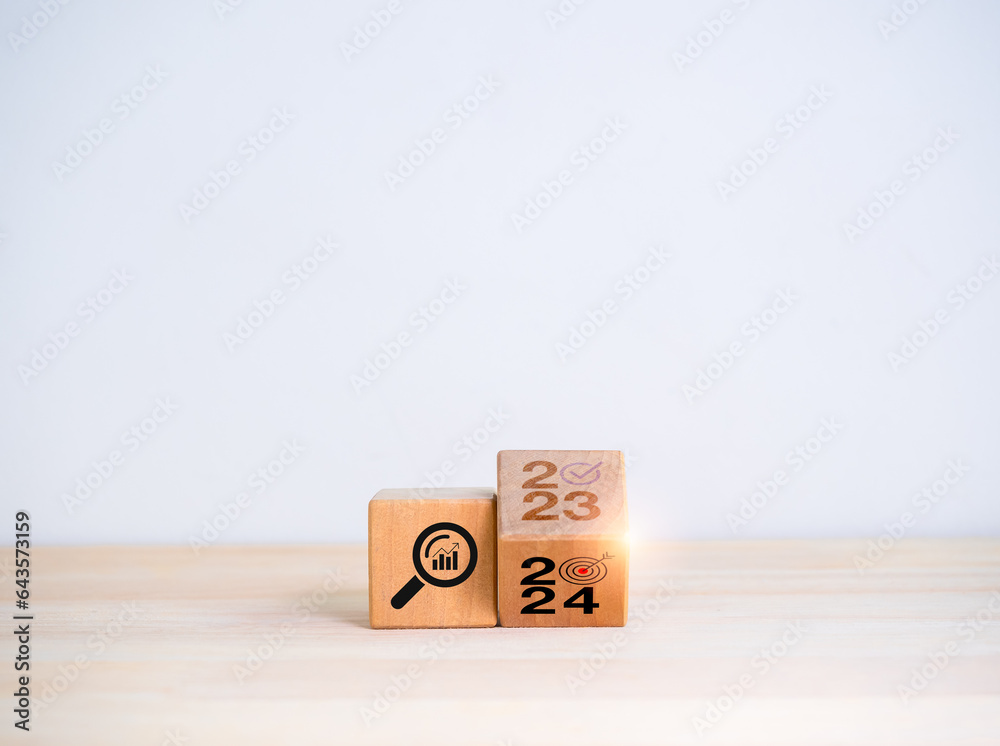 2024 new year trend concept. Flipping the 2023 to 2024 year numbers calendar and magnifying glass with graph, trends searching icon on wooden cube blocks isolated on white background with copy space. 2024 new year trend concept. Flipping the 2023 to 2024 year numbers calendar and magnifying glass with graph, trends searching icon on wooden cube blocks isolated on white background with copy space.
