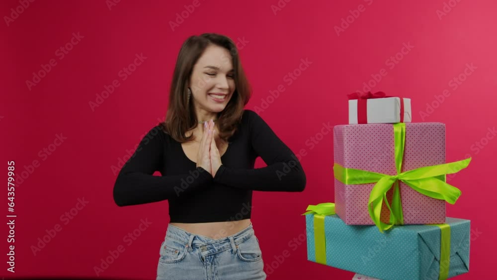 An elegant woman claps her hands, rejoicing at the gifts for the holiday. Beautifully packaged boxes are lying nearby. Red background An elegant woman claps her hands, rejoicing at the gifts for the holiday. Beautifully packaged boxes are lying nearby. Red background