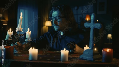 Shot capturing a priest sitting at the table, looking down with a candlestick and beads in his hands, prepared to perform a rite, ritual. photo