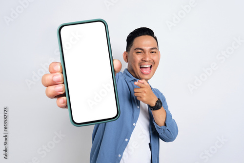 Excited young Asian man in casual shirt showing smartphone with blank screen isolated on white background photo