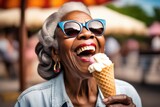 senior afro woman wearing sunglasses eating ice cream at amusement park