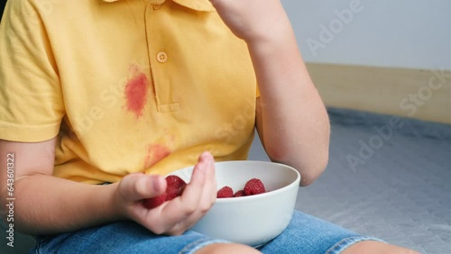Unrecognizable child eating raspberry with hands. Dirty berry stains on clothes and the skin of the hand. High quality 4k footage