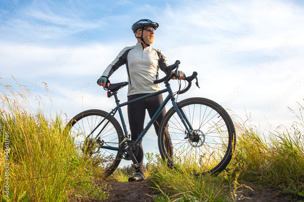 Bearded male cyclist is resting with a bike on the road in nature. cycling and health hobbies Bearded male cyclist is resting with a bike on the road in nature. cycling and health hobbies