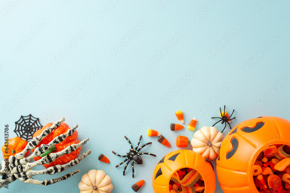 Festive trick or treat tradition for kids. Overhead shot displaying a pumpkin basket with candies and Halloween decorations on blue isolated background, suitable for text or ad placement
