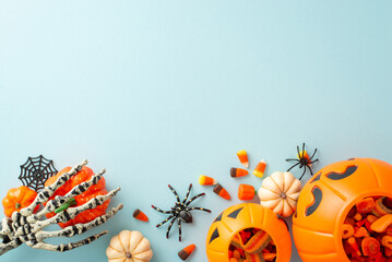Festive trick or treat tradition for kids. Overhead shot displaying a pumpkin basket with candies and Halloween decorations on blue isolated background, suitable for text or ad placement