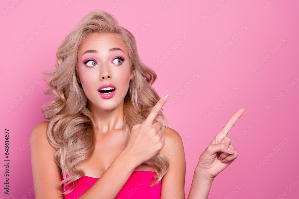 Photo of excited pretty lovely lady in doll style pointing finger emty space presenting adv promo on pink background Photo of excited pretty lovely lady in doll style pointing finger emty space presenting adv promo on pink background