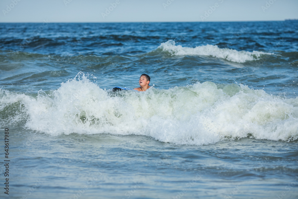 Cheerful teenage boy with a swimming board. Happy european family having fun floating on a swim board in the ocean on a hot summer day Cheerful teenage boy with a swimming board. Happy european family having fun floating on a swim board in the ocean on a hot summer day