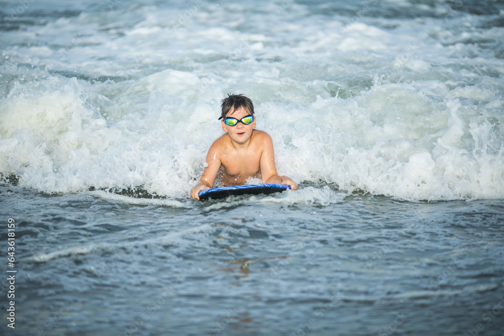 Little surfer learn to ride on surfboard on sea wave. Kid play in summer ocean, learning surfing, riding a wave. Little boy swim on kids surf board