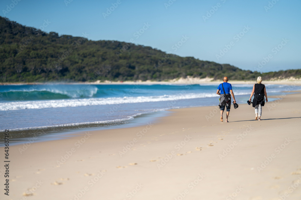 walking on Sandy beach, next to the sea with waves breaking behind, and mountains in the distance