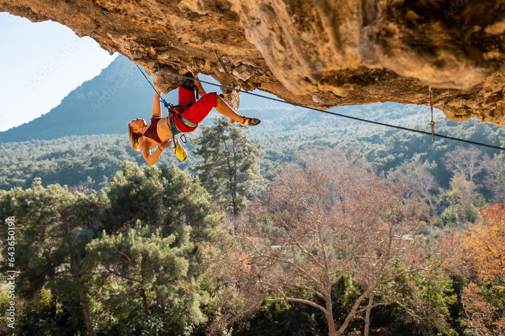 Obraz premium A young rock climber on an overhanging cliff. The climber climbs the rock. The girl is engaged in sports climbing.