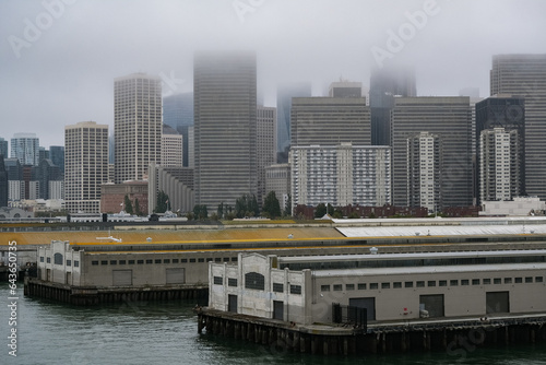 Grey foggy low hanging clouds day in San Francisco Bay with port piers, city skyline downtown architecture highrise buildings and landmarks as Coit Tower or Pyramid