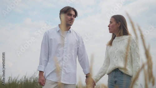 Portrait of confident man breaking up with woman leaving as sad stressed lady crossing hands looking away standing on the right in autumn field. Young Caucasian couple breakup photo