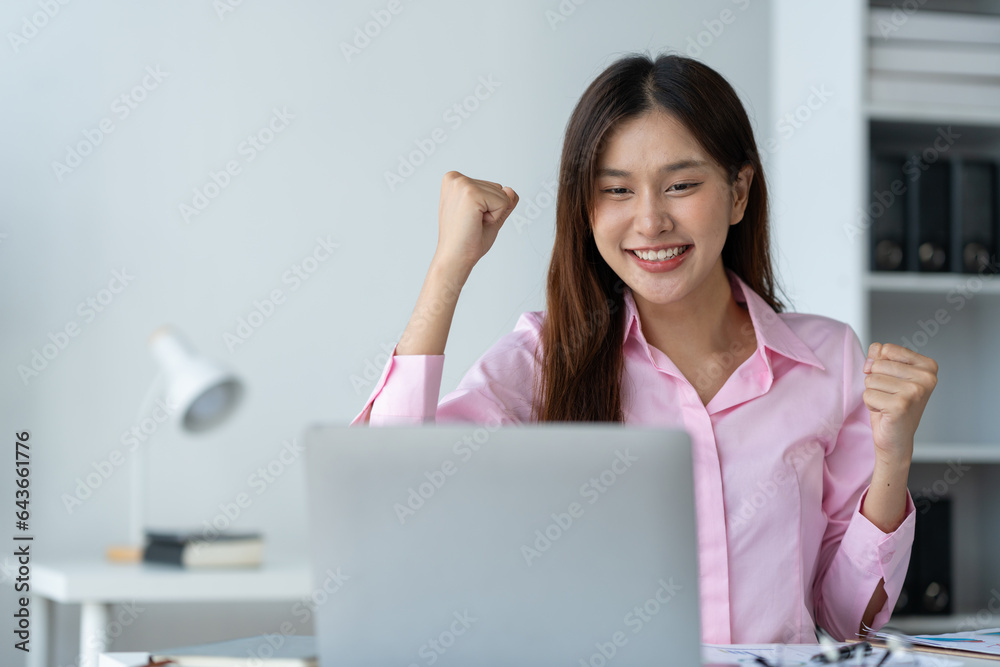 Asian businesswoman raising her hand with a happy expression and looking at her laptop.The businesswoman was delighted to receive an email informing her of her annual bonus. concept of success Asian businesswoman raising her hand with a happy expression and looking at her laptop.The businesswoman was delighted to receive an email informing her of her annual bonus. concept of success