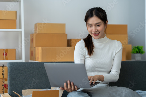 Asian businesswoman taking orders and checking online from laptop and mobile phone to prepare merchandise and deliver to customers in home office. business concept sme e-commerce freelance. © crizzystudio