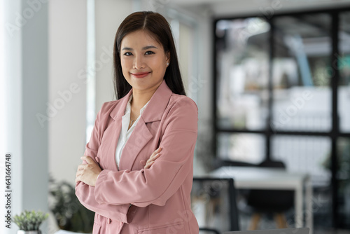 Young Asian businesswoman in casual suit happy smile While in modern office room with laptop about work in business administration, finance, accounting, marketing