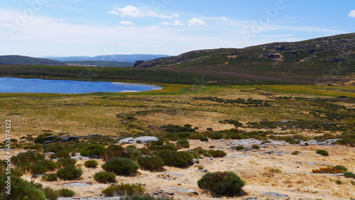 Chemin d'herbes ou de pailles jaunes, dans une zone de verdure, de bruyère et de rochers hispaniques, région montagneuses, balade naturelle et familiale, avec lac bleu à l'horizon, chaleur torride, photo