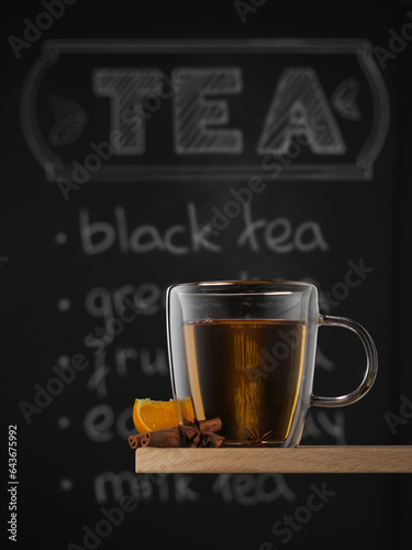 Clear glass mug with hot black tea, orange, cinnamone and anise against chalkboard background with tea written on it. photo
