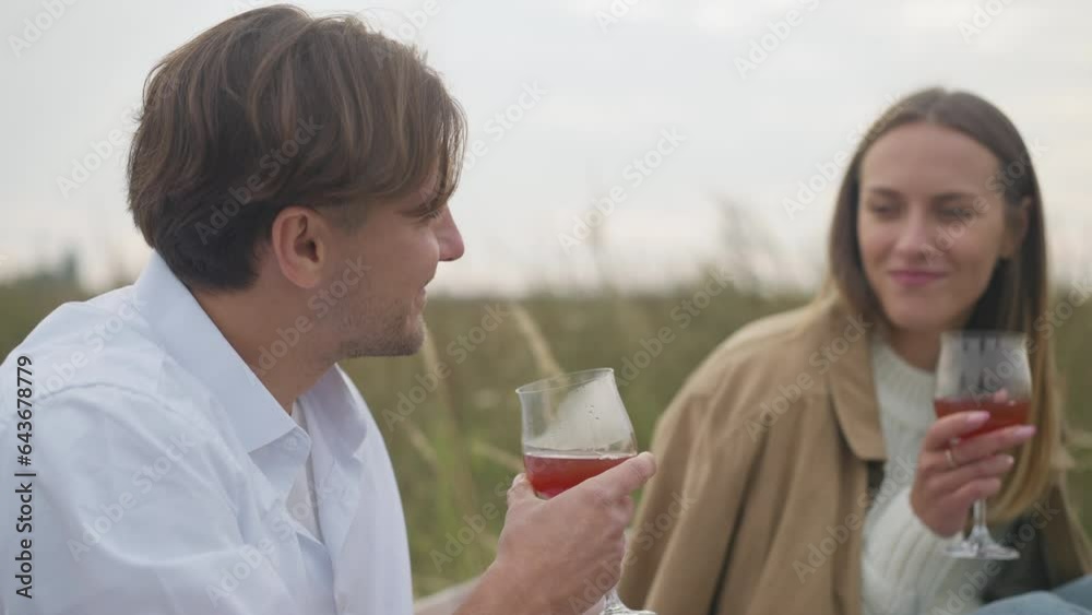 Side view smiling man toasting with blurred woman smelling red wine in glass. Happy loving handsome Caucasian husband on picnic with wife in cloudy autumn field Side view smiling man toasting with blurred woman smelling red wine in glass. Happy loving handsome Caucasian husband on picnic with wife in cloudy autumn field