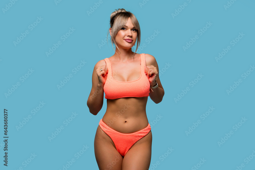 Naklejka premium Slim woman posing wearing orange swimsuit on blue background