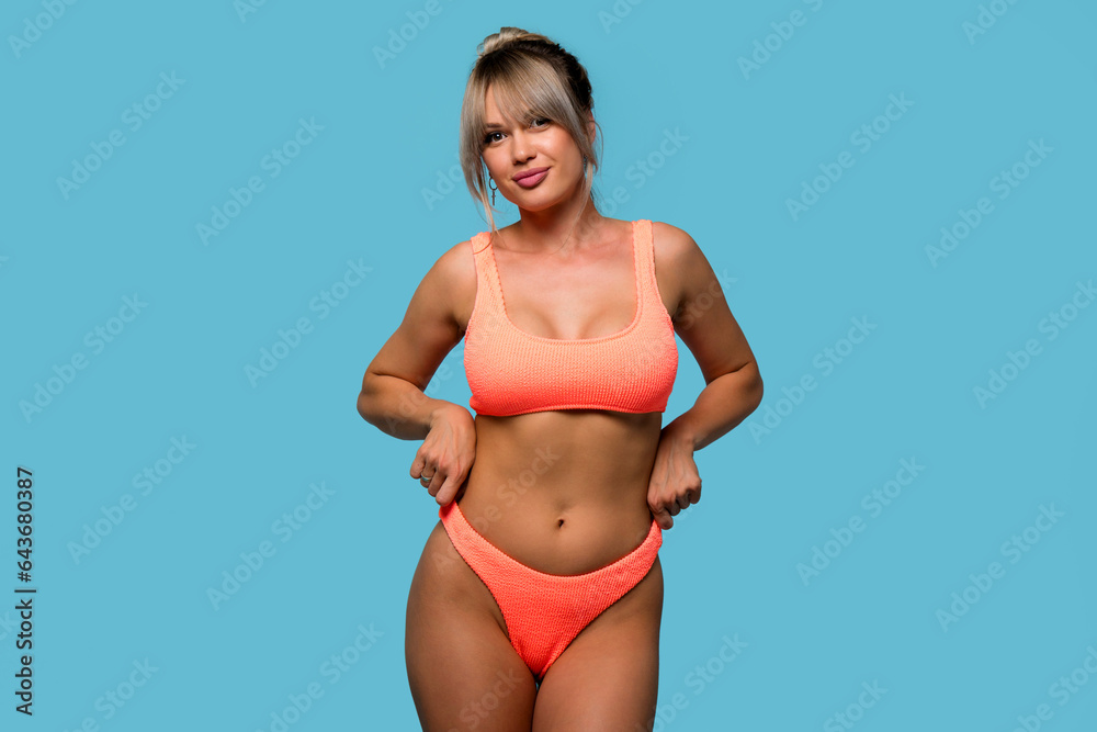 Naklejka premium Slim woman posing wearing orange swimsuit on blue background