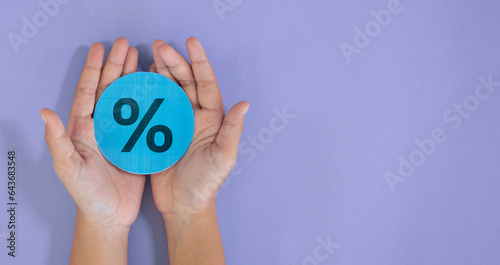 Hand holding circle cut paper with percentage interest icon on purple background. Finance and mortgage interest rates, banner concept with copy space.