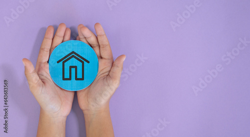 Hand holding paper cut circle with house icon on purple background. Financial interest rate and mortgage concept banner with copy space