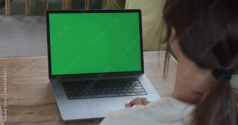 Over the shoulder shot woman using laptop with green screen while sitting in cafe. Business woman at coffee shop working on a Laptop Computer with Green Mock-up Screen. Chroma key, copy space.