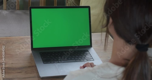 Over the shoulder shot woman using laptop with green screen while sitting in cafe. Business woman at coffee shop working on a Laptop Computer with Green Mock-up Screen. Chroma key, copy space.