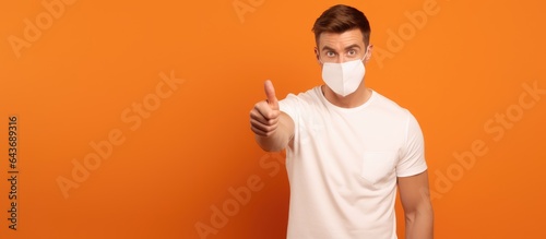 Brunette man with medical mask pointing left isolated on orange background