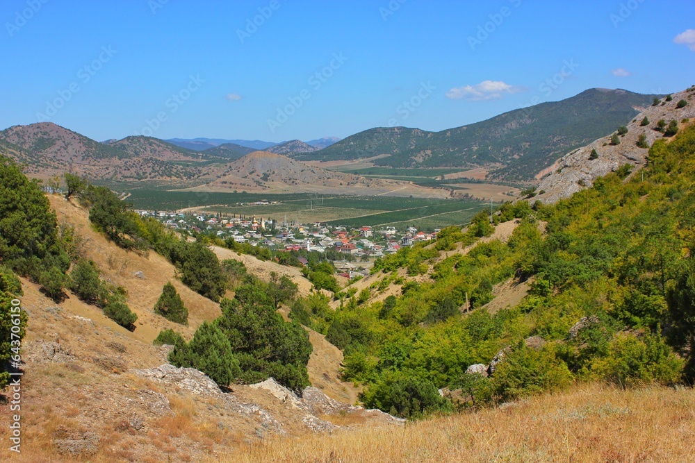View of a small town Through the gorge  lost among green hills and rocks. Point summer day, blue sky, a pleasant place for tourism. View from the gorge.