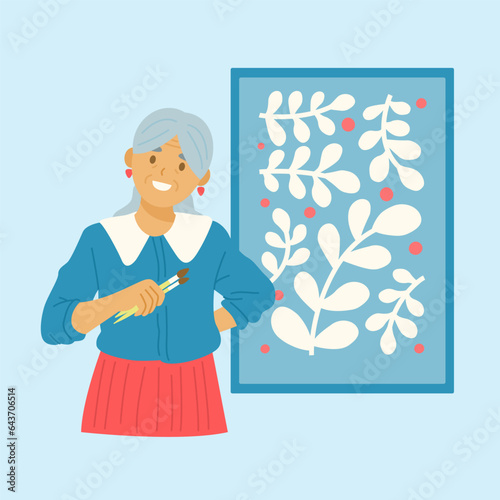 Elderly woman with brushes in her hands stands against the background of her painting.