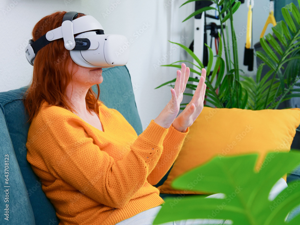 woman sitting on sofa relaxing and playing VR and using futuristic artificial intelligence at home.. the concept of metaverse, virtual reality, future, technology, and internet of things.
