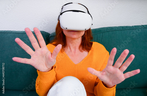 Obraz na płótnie woman sitting on sofa relaxing and playing VR and using futuristic artificial intelligence at home.. the concept of metaverse, virtual reality, future, technology, and internet of things. w salonie