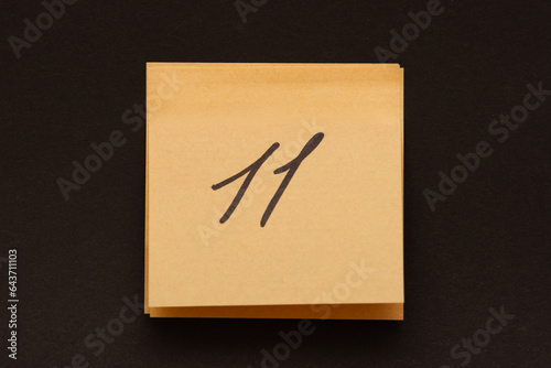 The number eleven is written on a self-adhesive sheet of paper, a sticker, on a dark background photo