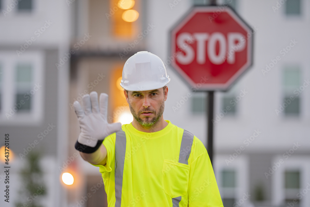Worker builder in hard hat with stop road sign. Builder with stop gesture, no hand, dangerous on building concept. Man in worker uniform and hardhat with open hand doing stop sign. Worker builder in hard hat with stop road sign. Builder with stop gesture, no hand, dangerous on building concept. Man in worker uniform and hardhat with open hand doing stop sign.
